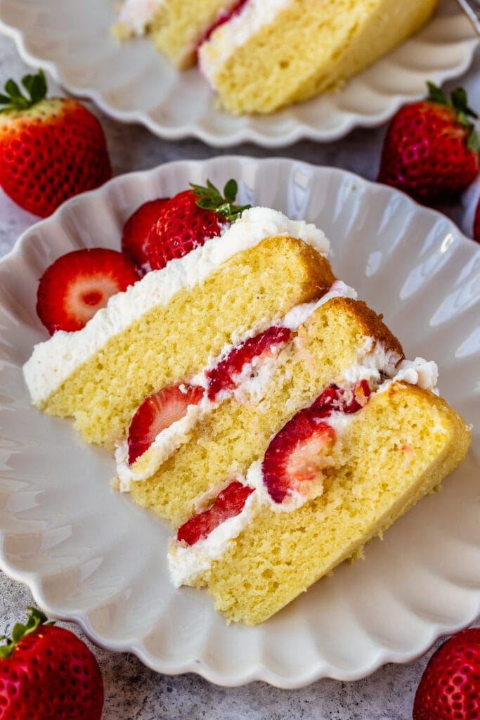 slice of strawberry shortcake cake on a plate, with whipped cream and fresh strawberries in the middle.