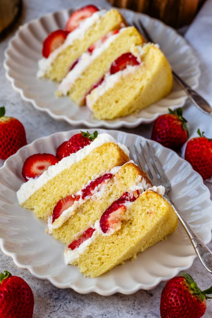 slice of strawberry cream cake on a plate, with whipped cream and fresh strawberries in the middle.