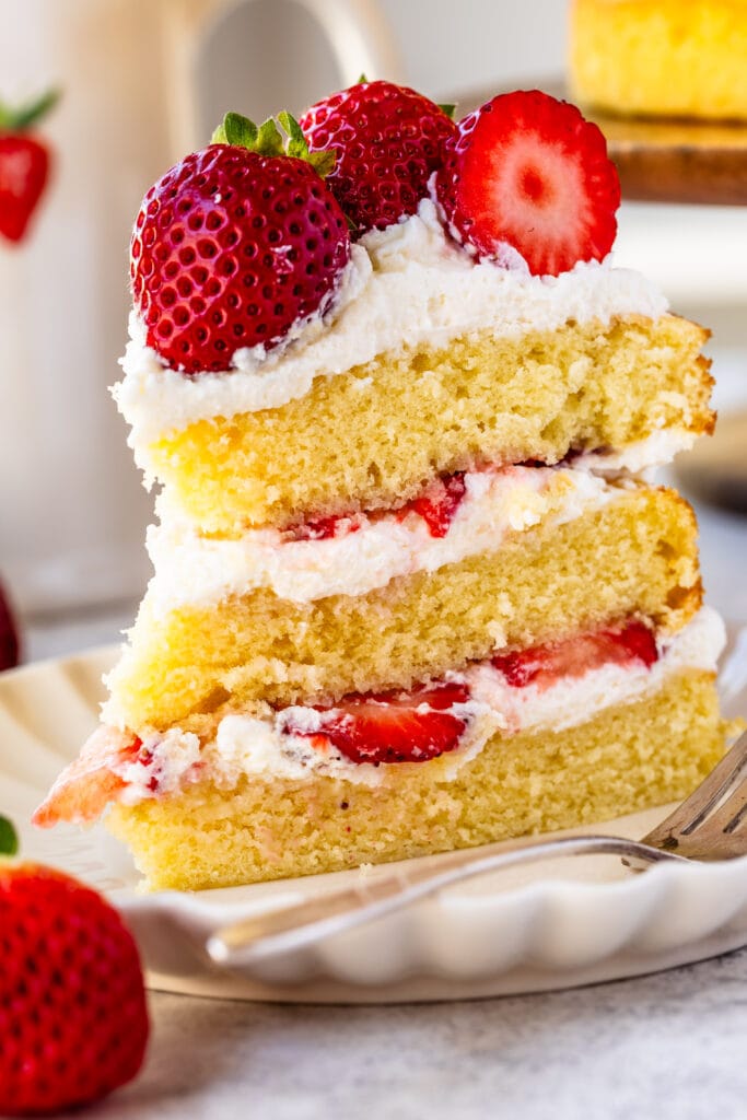 slice of strawberry shortcake cake on a plate, with whipped cream and fresh strawberries in the middle.