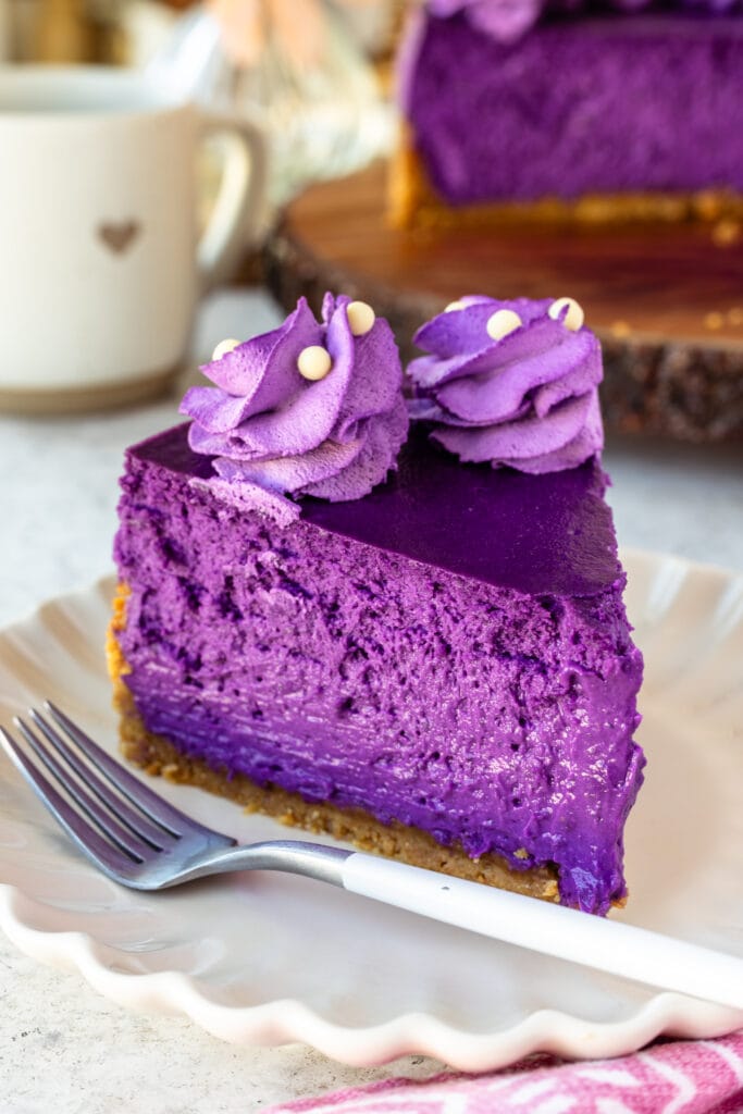 slice of ube purple cheesecake on a plate, with purple whipped cream on top.