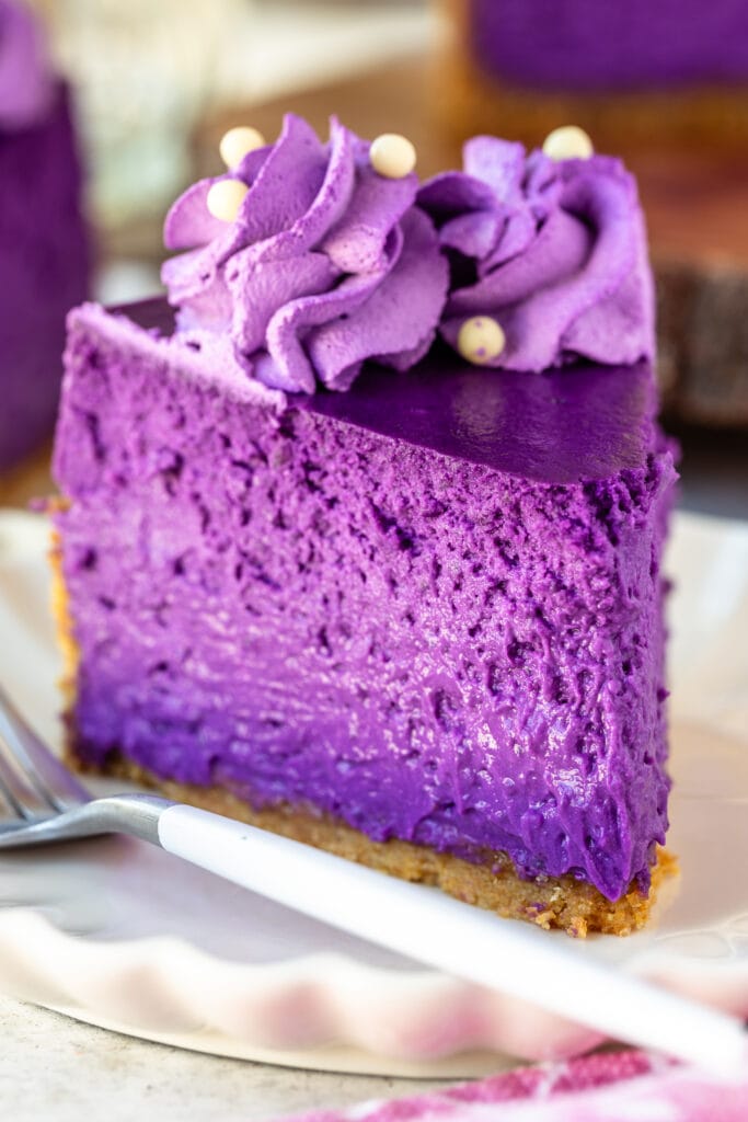 slice of ube purple cheesecake on a plate, with purple whipped cream on top.