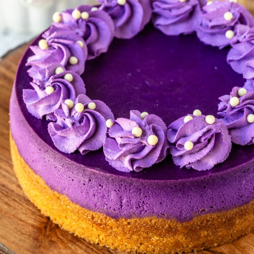 Ube cheesecake, a purple cheesecake with purple whipped cream piped on top, on top of a wooden board.
