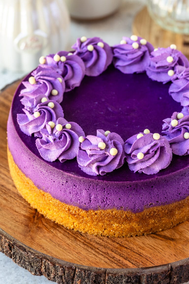 Ube cheesecake, a purple cheesecake with purple whipped cream piped on top, on top of a wooden board.