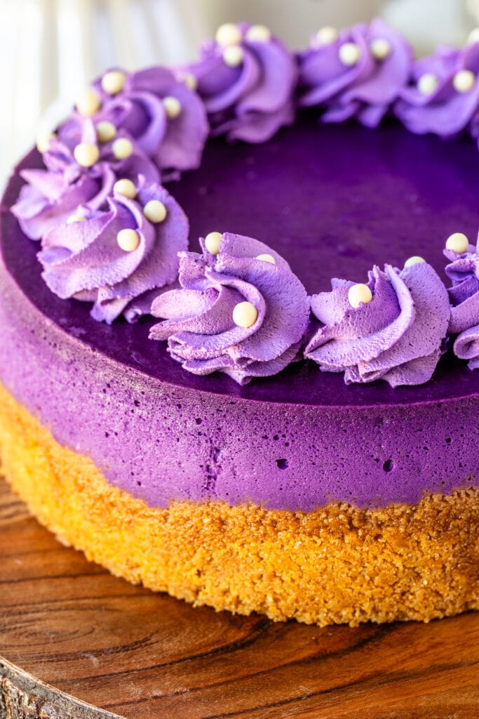 Ube purple cheesecake with purple whipped cream piped on top, on top of a wooden board.