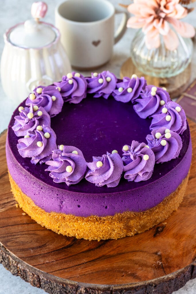 Ube cheesecake, a purple cheesecake with purple whipped cream piped on top, on top of a wooden board.