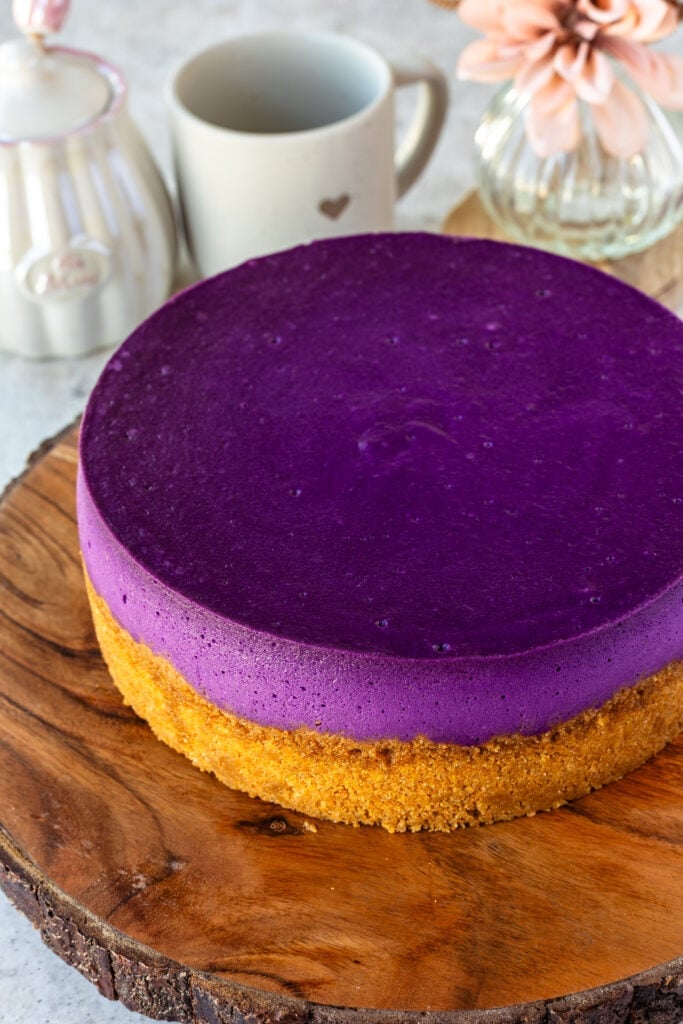 purple cheesecake on a graham cracker crust on a wooden board.