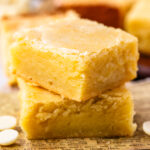 two pieces of white chocolate brownies stacked on top of each other on a wooden board.