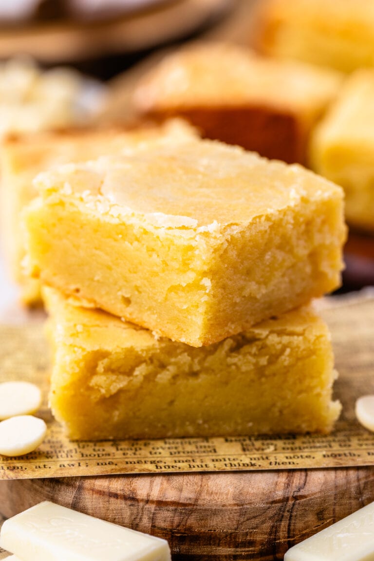 two pieces of white chocolate brownies stacked on top of each other on a wooden board.