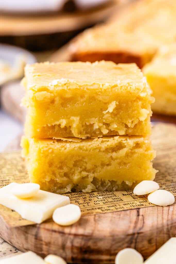 two pieces of white chocolate brownies stacked on top of each other on a wooden board.