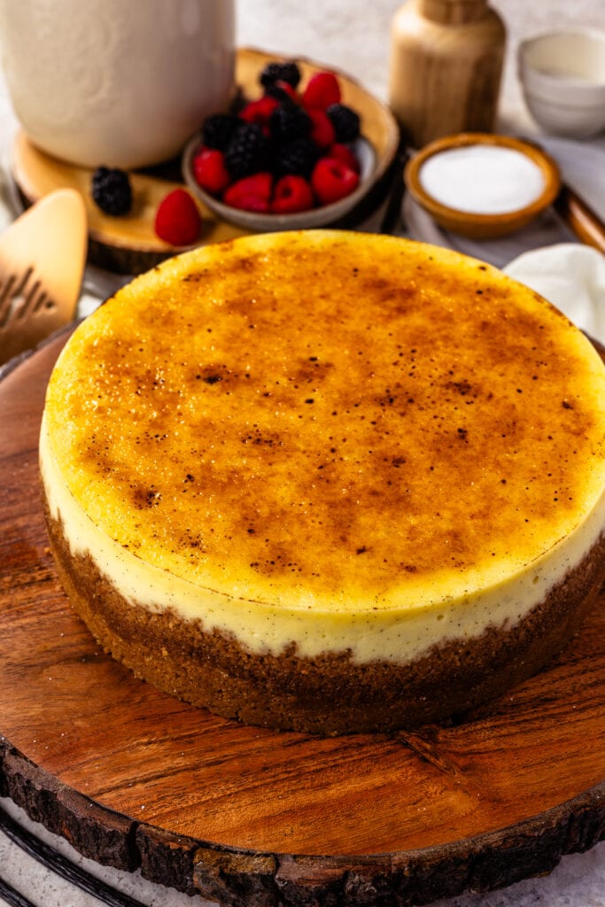 creme brulee cheesecake on top of a wooden board, with a caramelized sugar topping, and berries on the back.