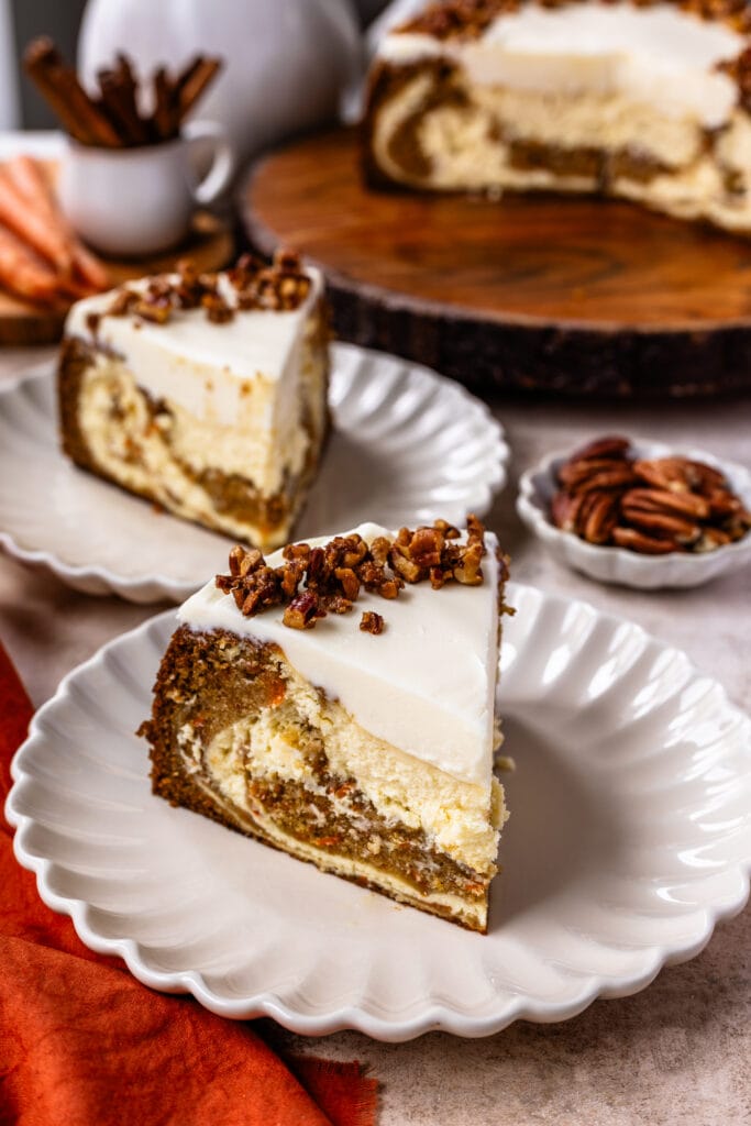 two slices of carrot cake cheesecake on plates, with a sliced cheesecake on the back.