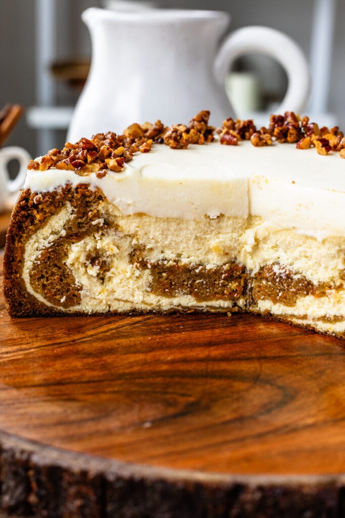 sliced carrot cake cheesecake topped with cream cheese frosting and candied pecans on top.