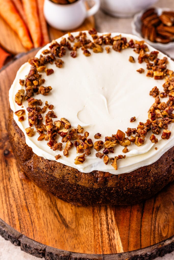 carrot cake cheesecake topped with cream cheese frosting and candied pecans on top.