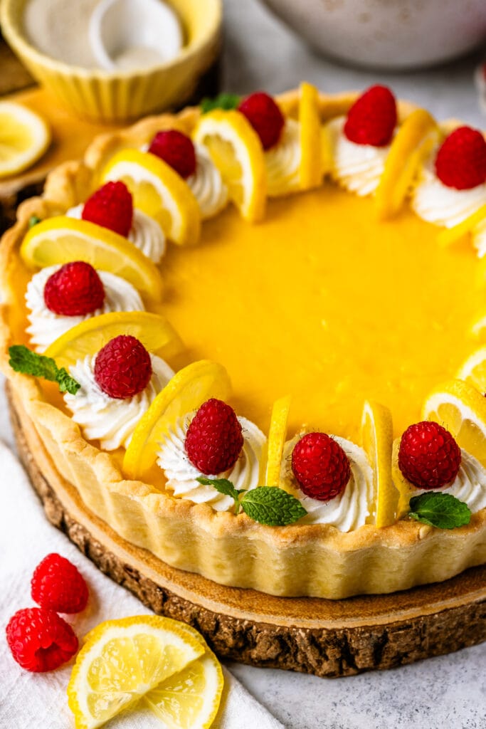 Lemon pie with raspberries and lemon slices on top, on a wooden board.