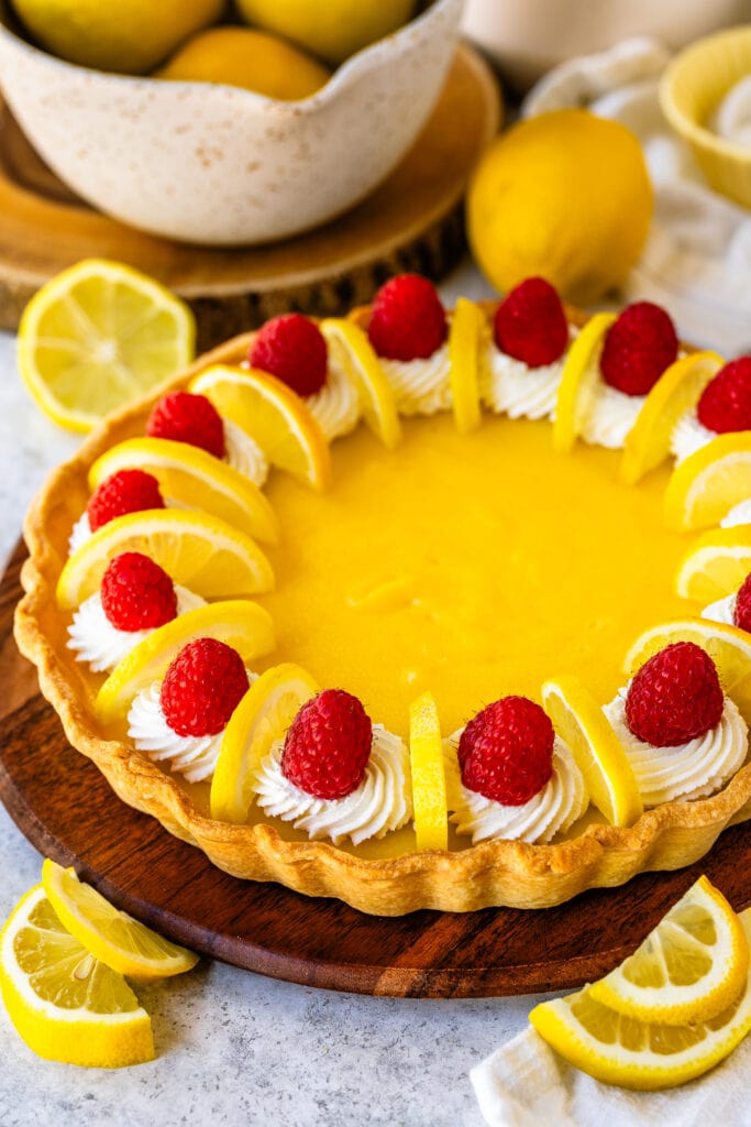 Lemon pie with raspberries and lemon slices on top, on a wooden board.