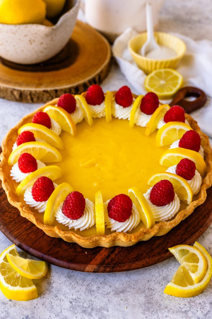 Lemon Tart with raspberries and lemon slices on top, on a wooden board.