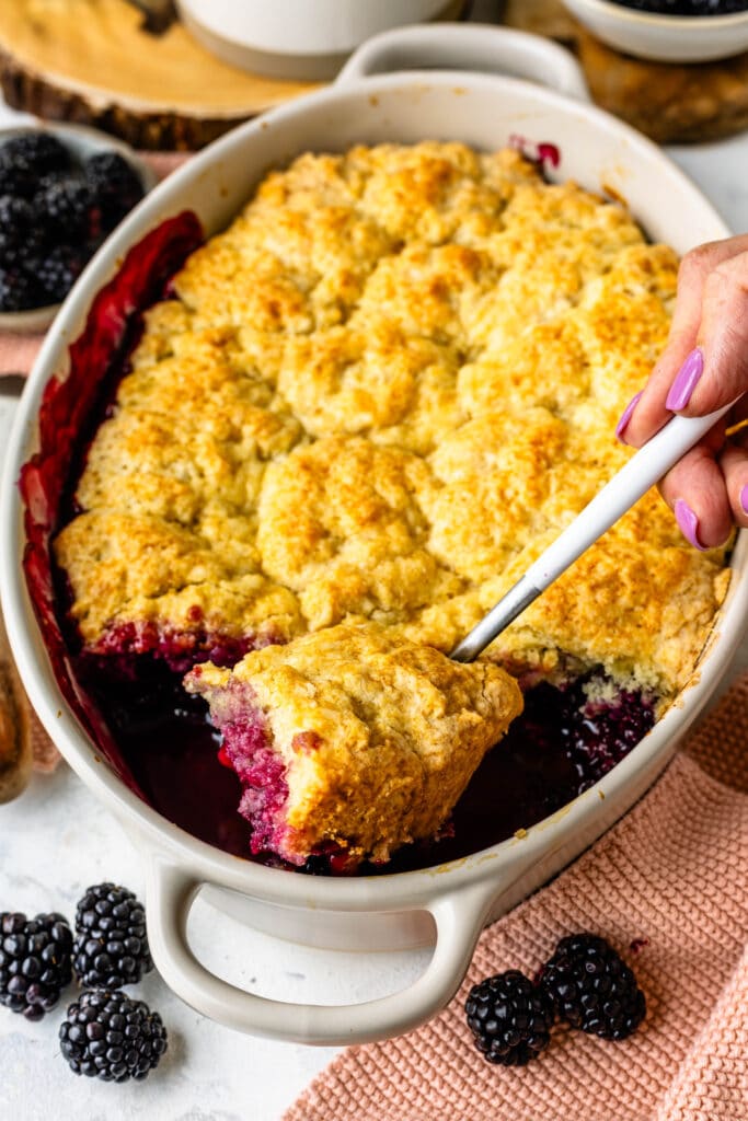 hand removing some blackberry cobbler from the pan.