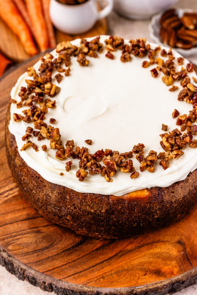 carrot cake cheesecake topped with cream cheese frosting and candied pecans on top.