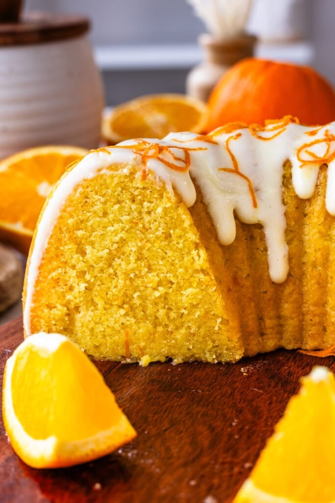 orange bundt cake sliced, on top of a board, with orange slices around.