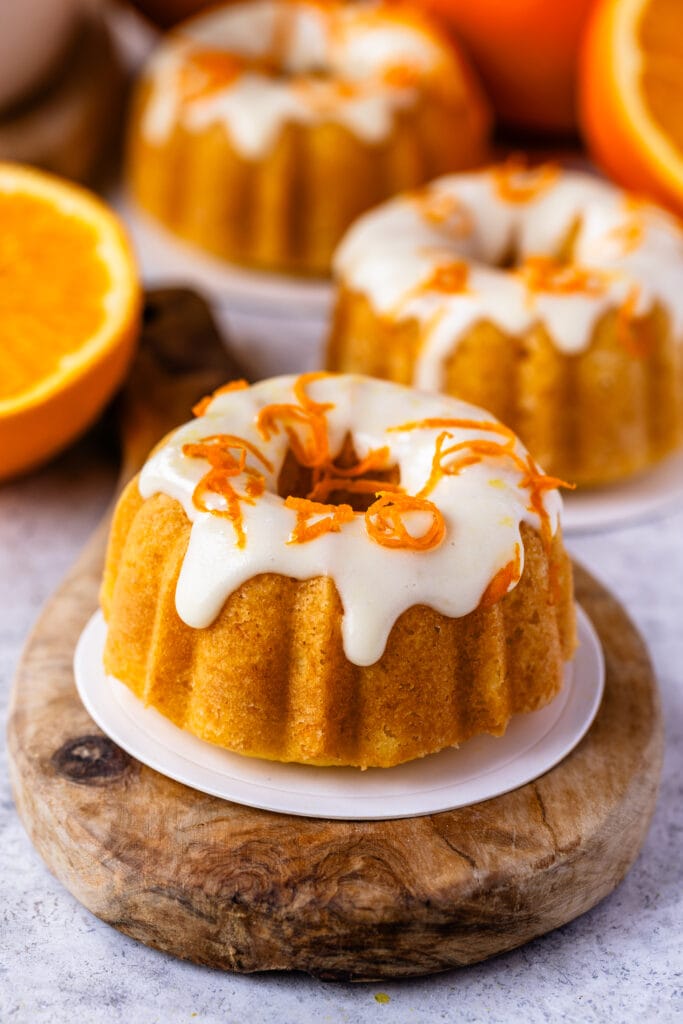 mini orange bundt cake on top of a wooden board, with glaze and orange zest on top.