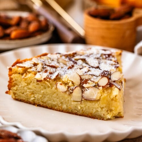 almond cake slice on a plate, topped with sliced almonds and powdered sugar.