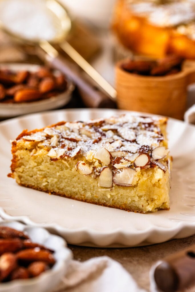 almond cake slice on a plate, topped with sliced almonds and powdered sugar.