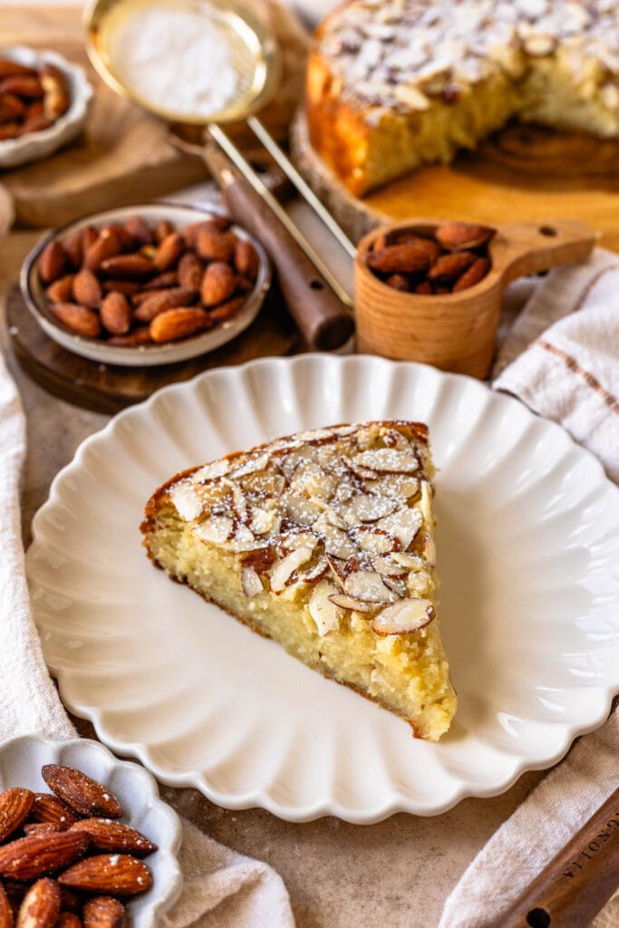 almond cake slice on a plate, topped with sliced almonds and powdered sugar.