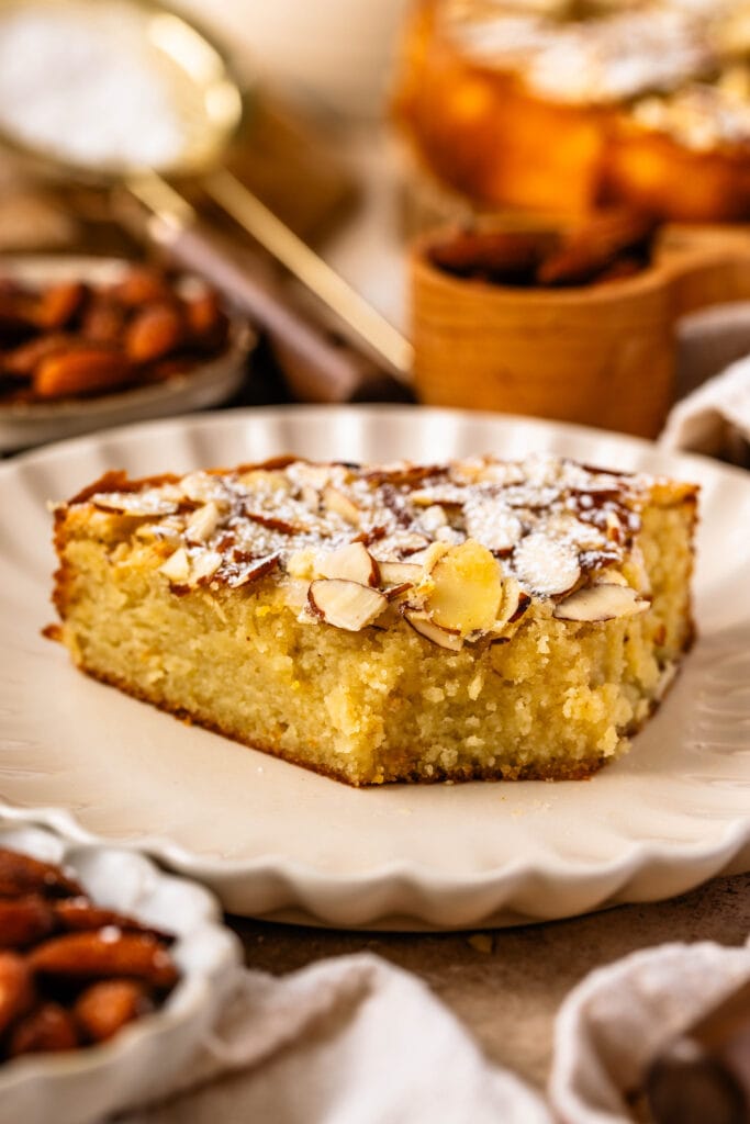 almond cake slice on a plate, topped with sliced almonds and powdered sugar.