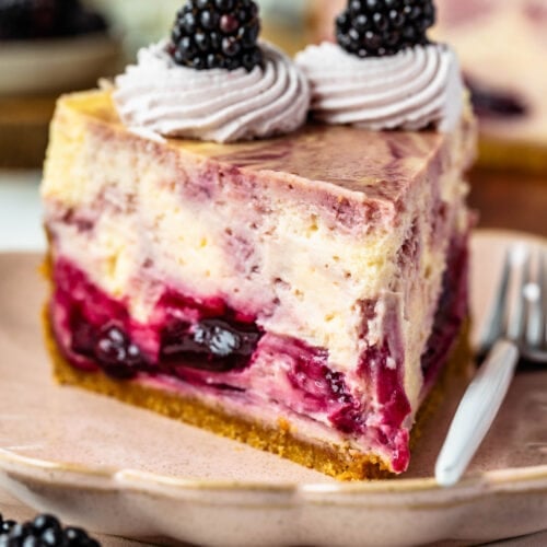 slice of blackberry cheesecake with graham cracker crust, and blackberry sauce mixed into the cheesecake batter, with whipped cream on top and blackberry.