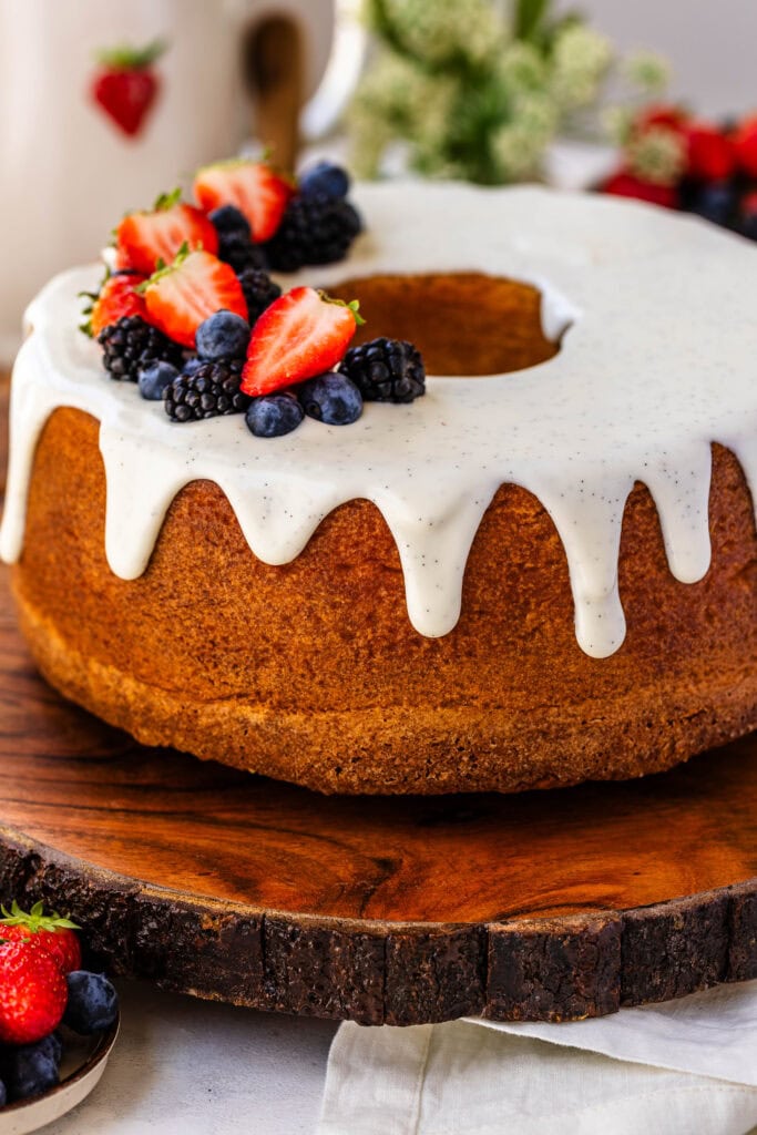 Cream Cheese Pound Cake with cream cheese vanilla bean glaze on top, and fresh strawberries, and blueberries and blackberries on top of the cake, that's on top of a wooden board.