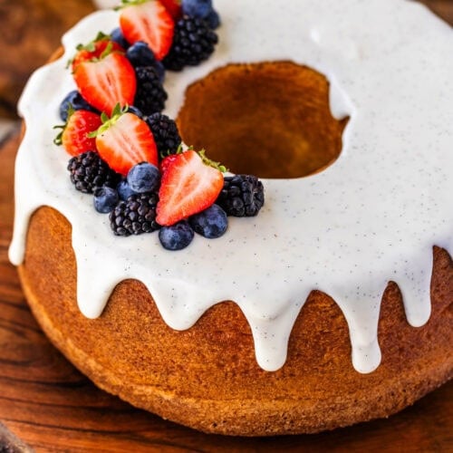 Cream Cheese Pound Cake with cream cheese vanilla bean glaze on top, and fresh strawberries, and blueberries and blackberries on top of the cake, that's on top of a wooden board.