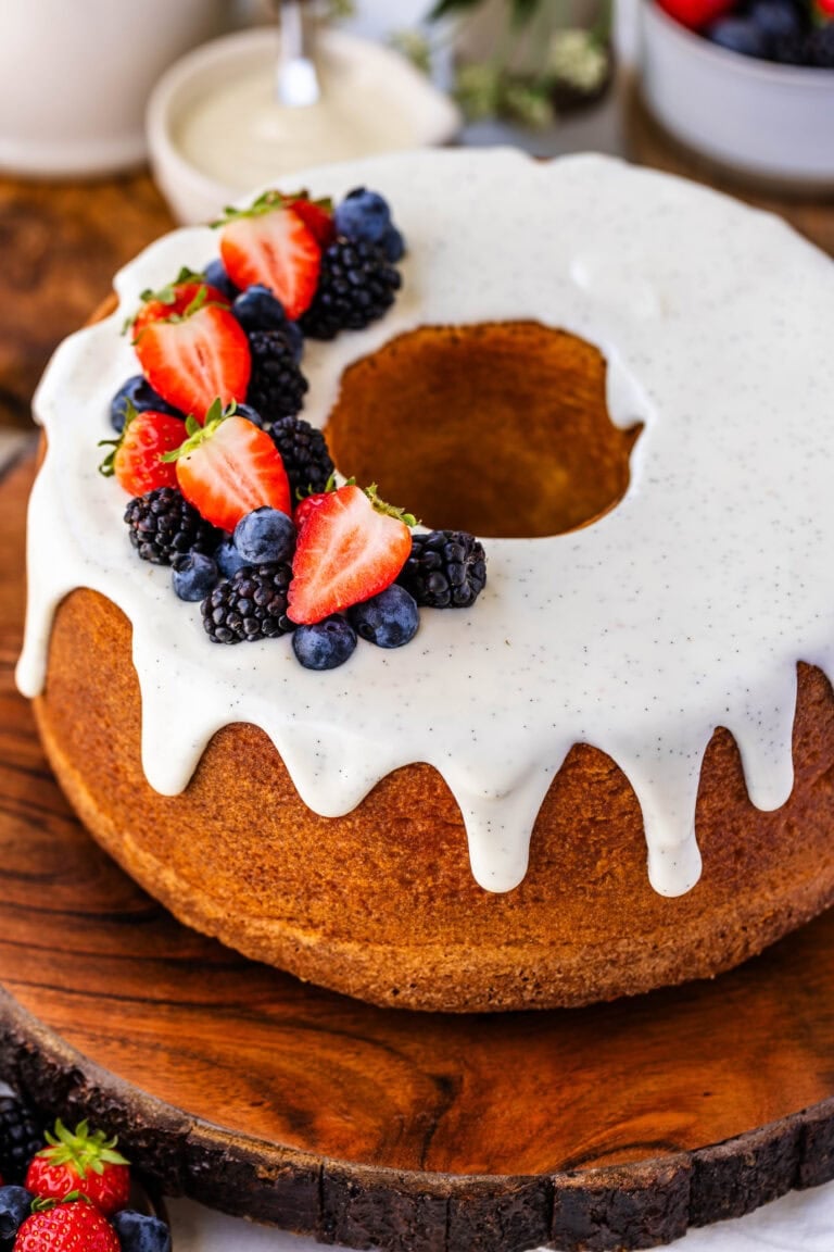 Cream Cheese Pound Cake with cream cheese vanilla bean glaze on top, and fresh strawberries, and blueberries and blackberries on top of the cake, that's on top of a wooden board.