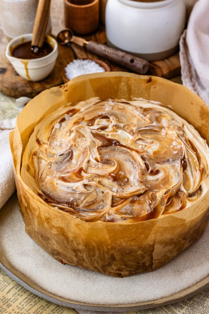 caramel cake in parchment paper with caramel swirls and cream cheese frosting on top.