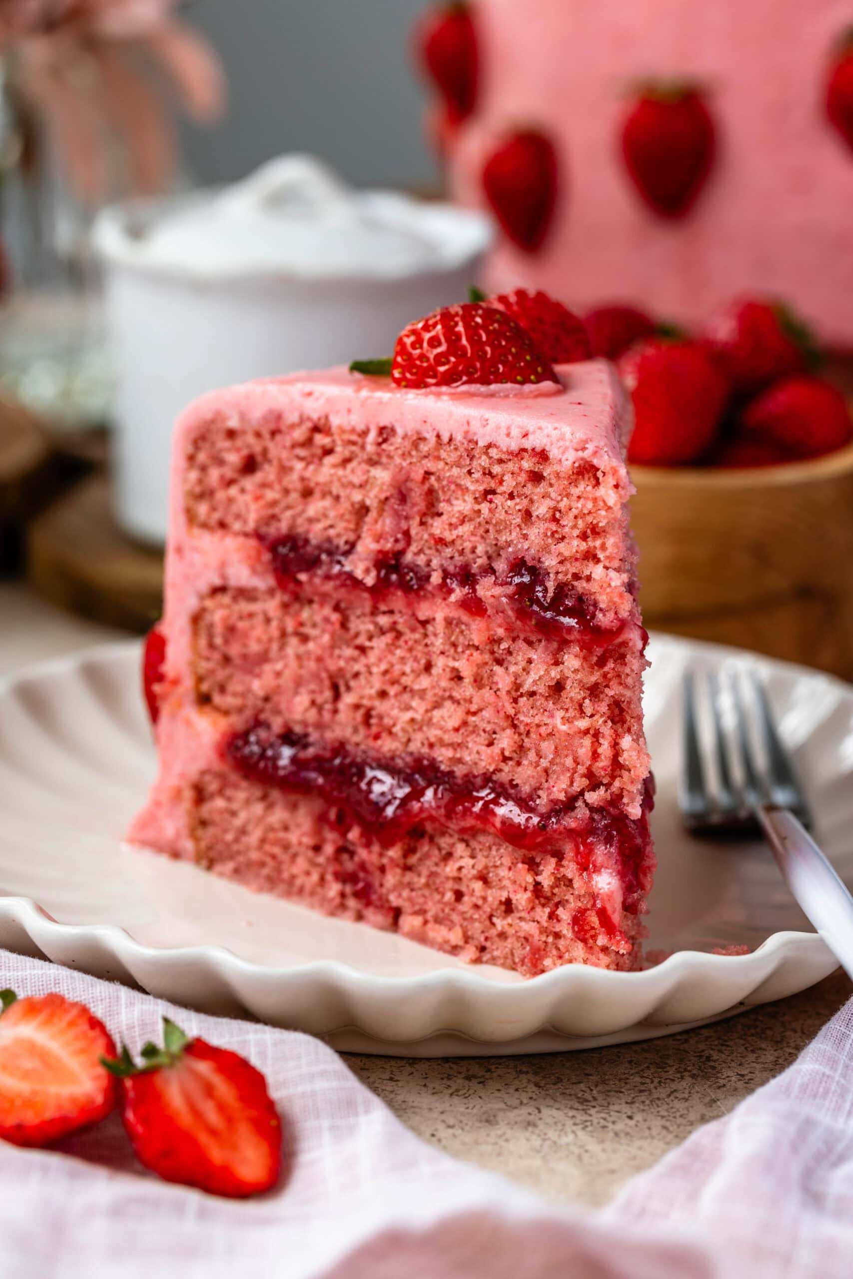 Slice of strawberry layer cake with strawberry jam filling and cream cheese frosting on a plate