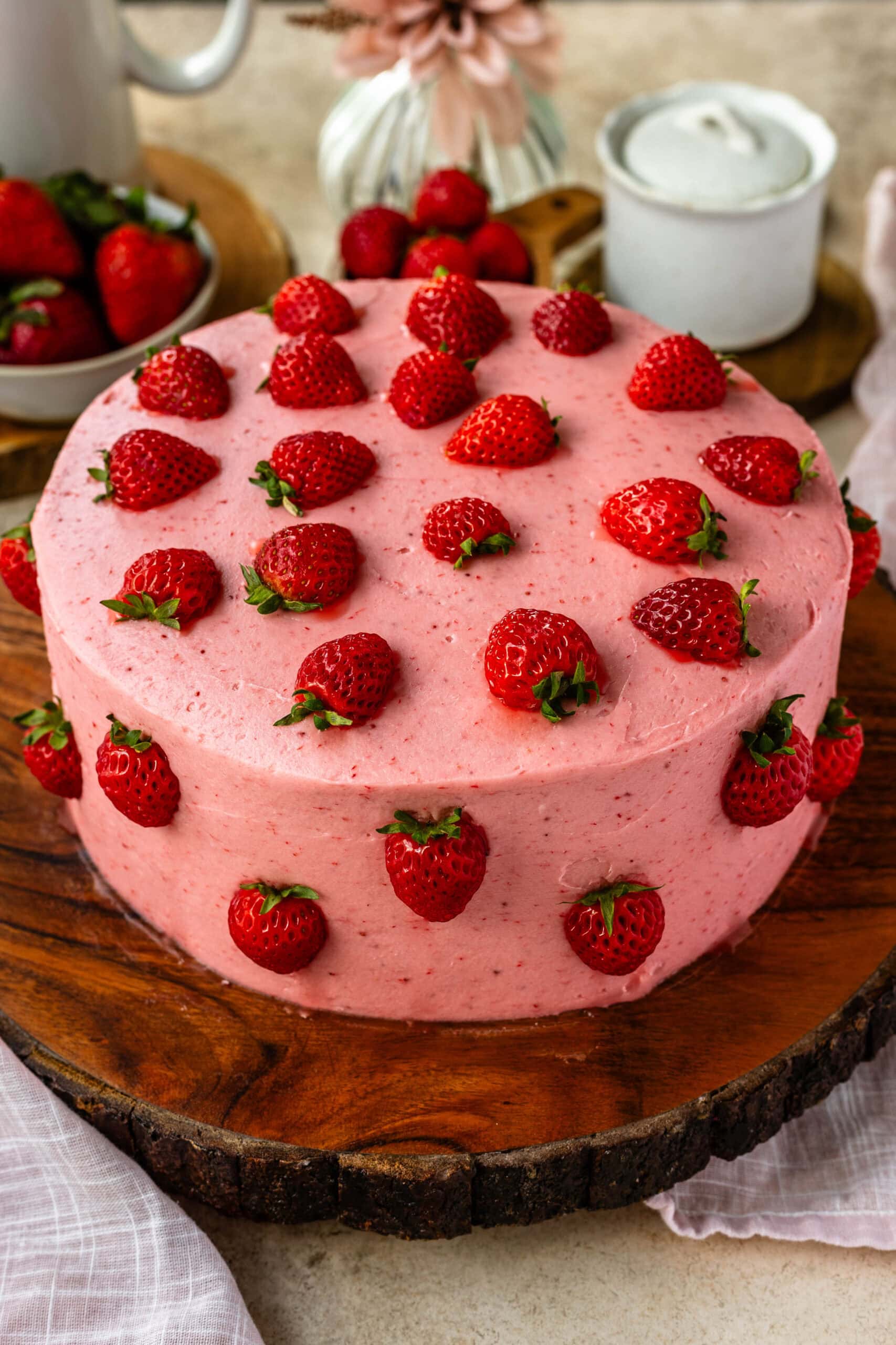 strawberry cake, a pink cake on top of a wooden board, the cake has pink frosting and is decorated with halved strawberries.