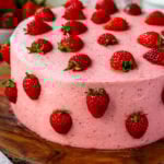 strawberry cake, a pink cake on top of a wooden board, the cake has pink frosting and is decorated with halved strawberries.