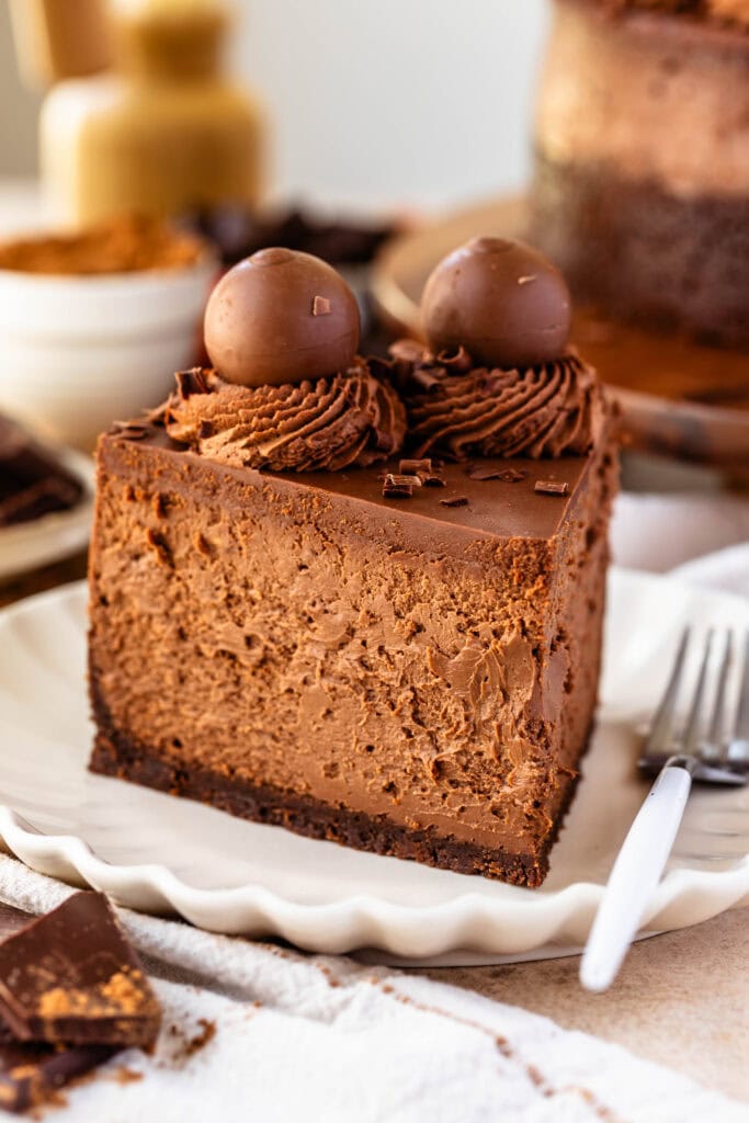 slice of chocolate cheesecake topped with truffles and whipped cream on a plate, with a fork next to it.