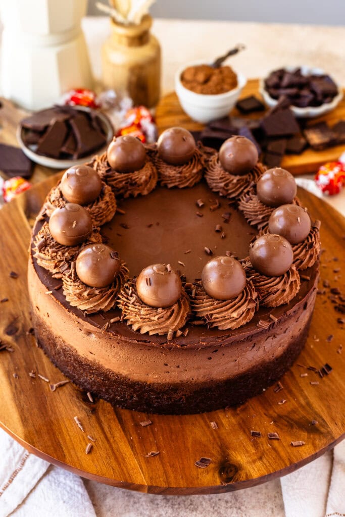 Chocolate cheesecake with chocolate whipped cream on top and chocolate truffles, on top of a wooden board.