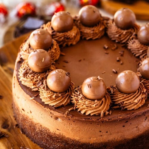 Chocolate cheesecake with chocolate whipped cream on top and chocolate truffles, on top of a wooden board.