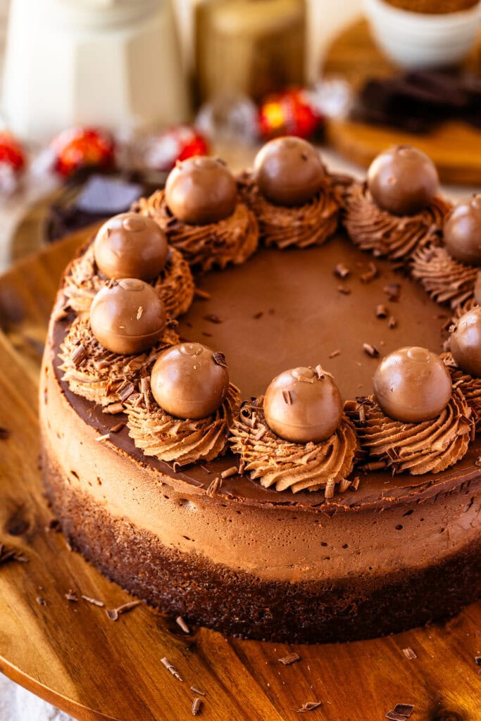 Chocolate cheesecake with chocolate whipped cream on top and chocolate truffles, on top of a wooden board.