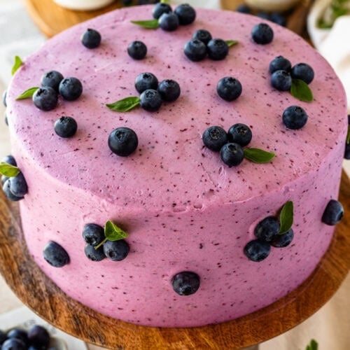 blueberry cake frosted with blueberry frosting, with fresh blueberries decorating the cake.