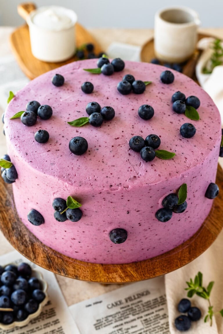 blueberry cake frosted with blueberry frosting, with fresh blueberries decorating the cake.