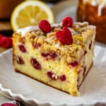 slice of lemon raspberry cake with glaze and crumble on top, and raspberries on top of the cake slice.