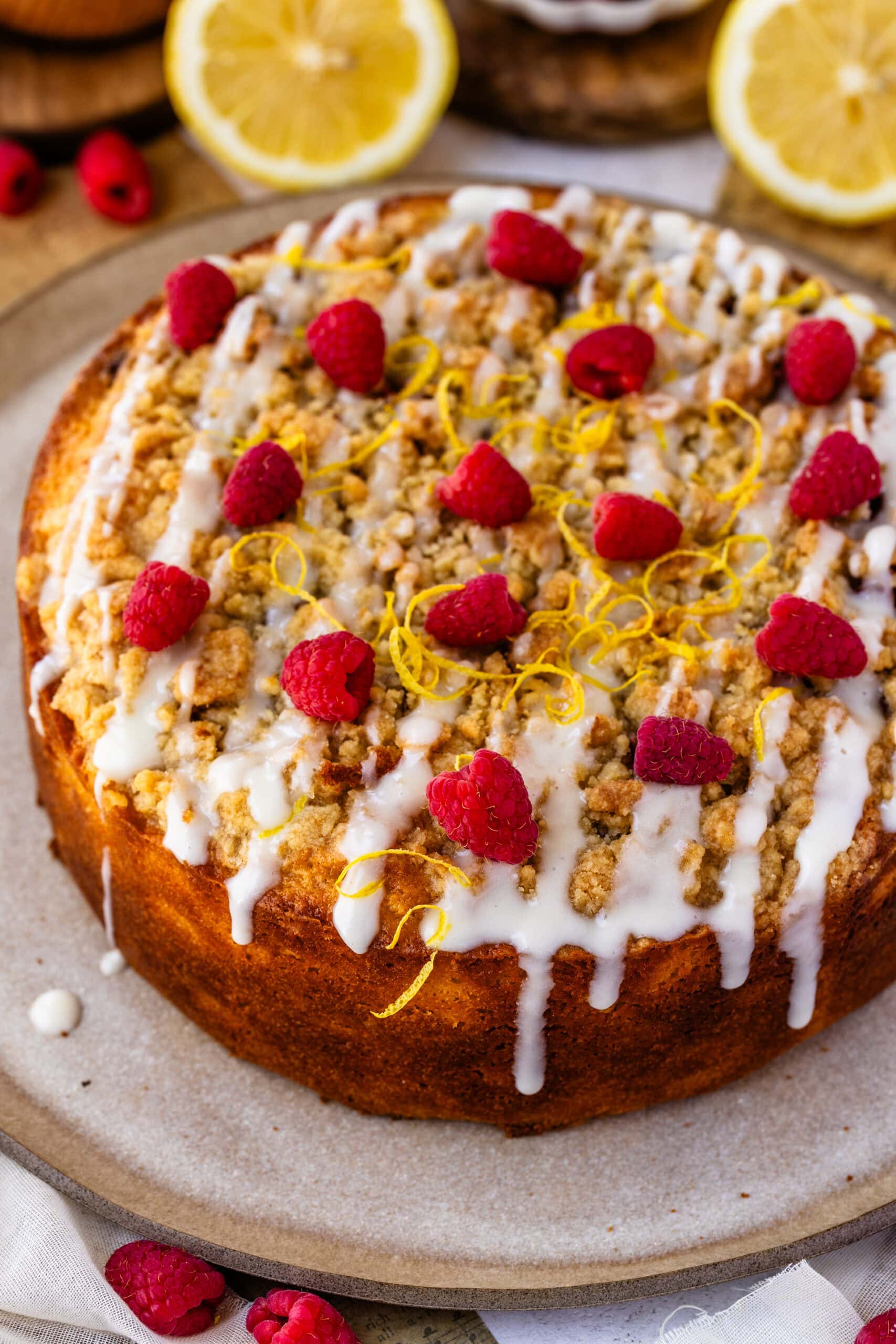lemon raspberry cake on a plate drizzled with glaze, topped with raspberries and lemon zest.