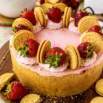 strawberry cheesecake, with whipped cream on top, strawberries, and oreos, on top of a wooden board.