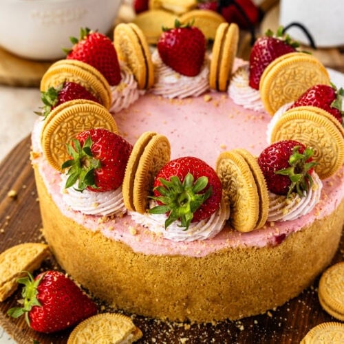 strawberry cheesecake, with whipped cream on top, strawberries, and oreos, on top of a wooden board.