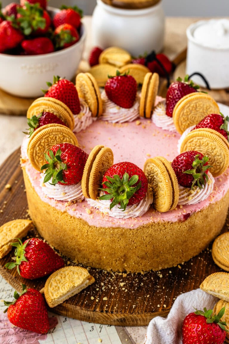 strawberry cheesecake, with whipped cream on top, strawberries, and oreos, on top of a wooden board.