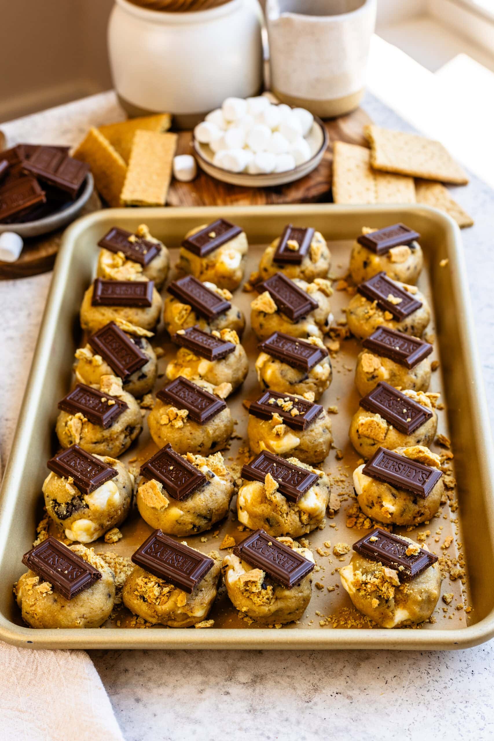 baking tray with smores cookie dough on top of it, with hersheys chocolate pieces on top.