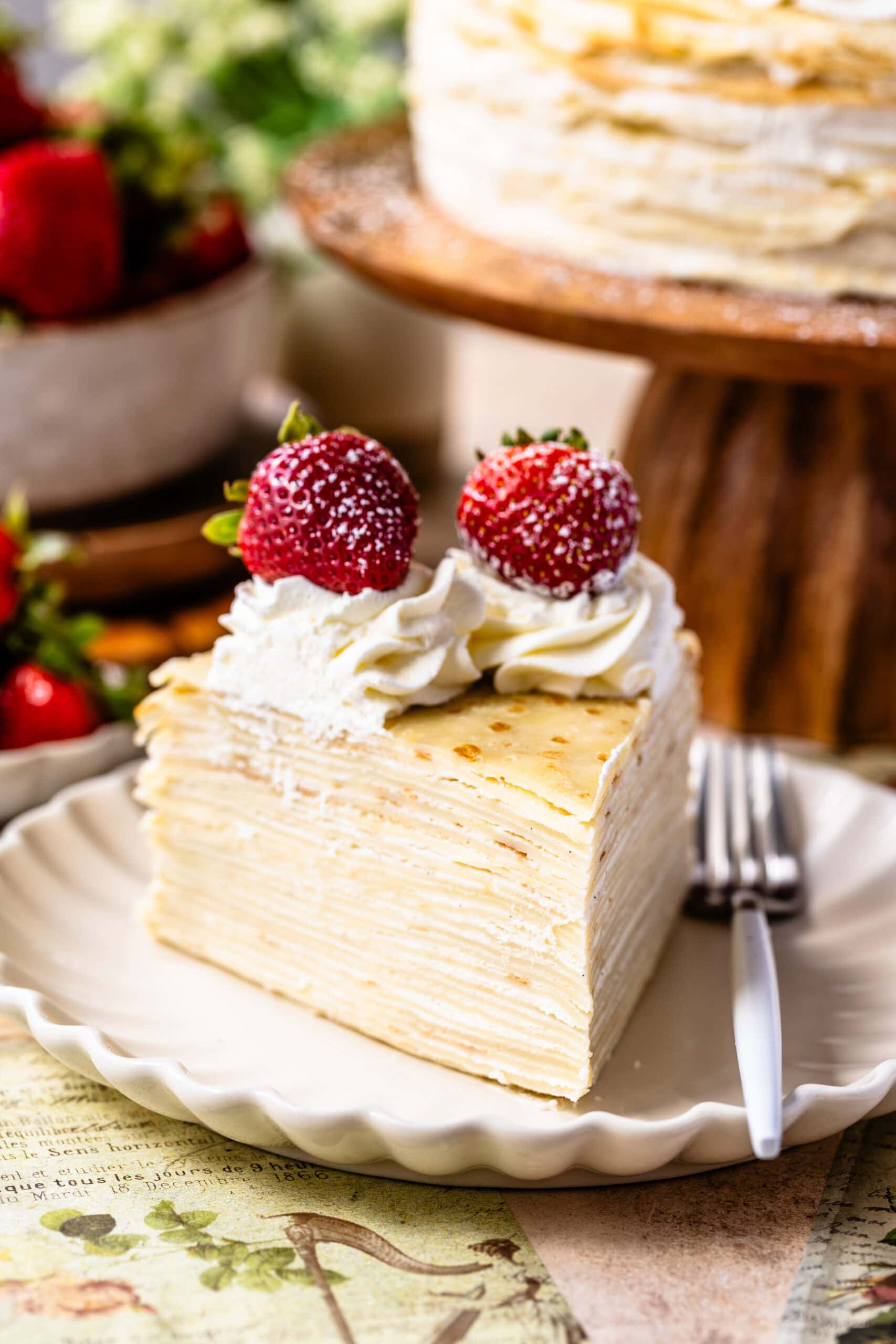 slice of crepe cake on a plate with strawberries and whipped cream on top.