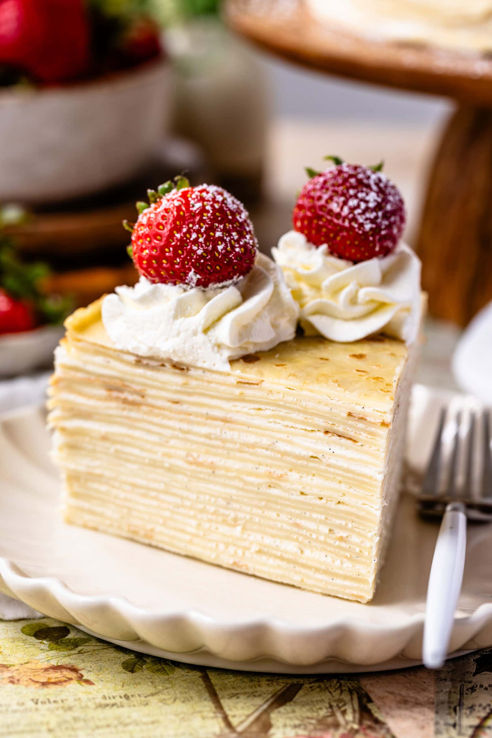 slice of crepe cake on a plate with strawberries and whipped cream on top.